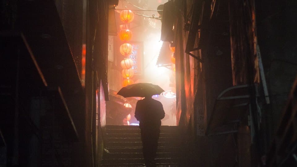 Photograph of a man walking up stairs holding an umbrella, shot from low angle