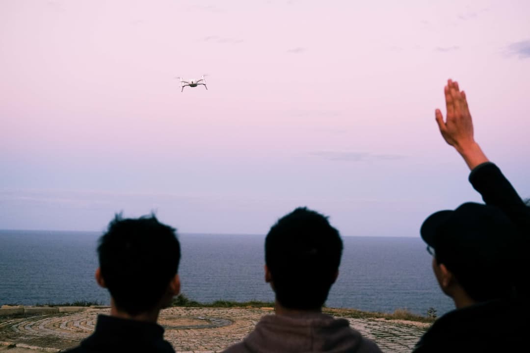 Landscape photo of 3 men looking up at a nearby flying drone